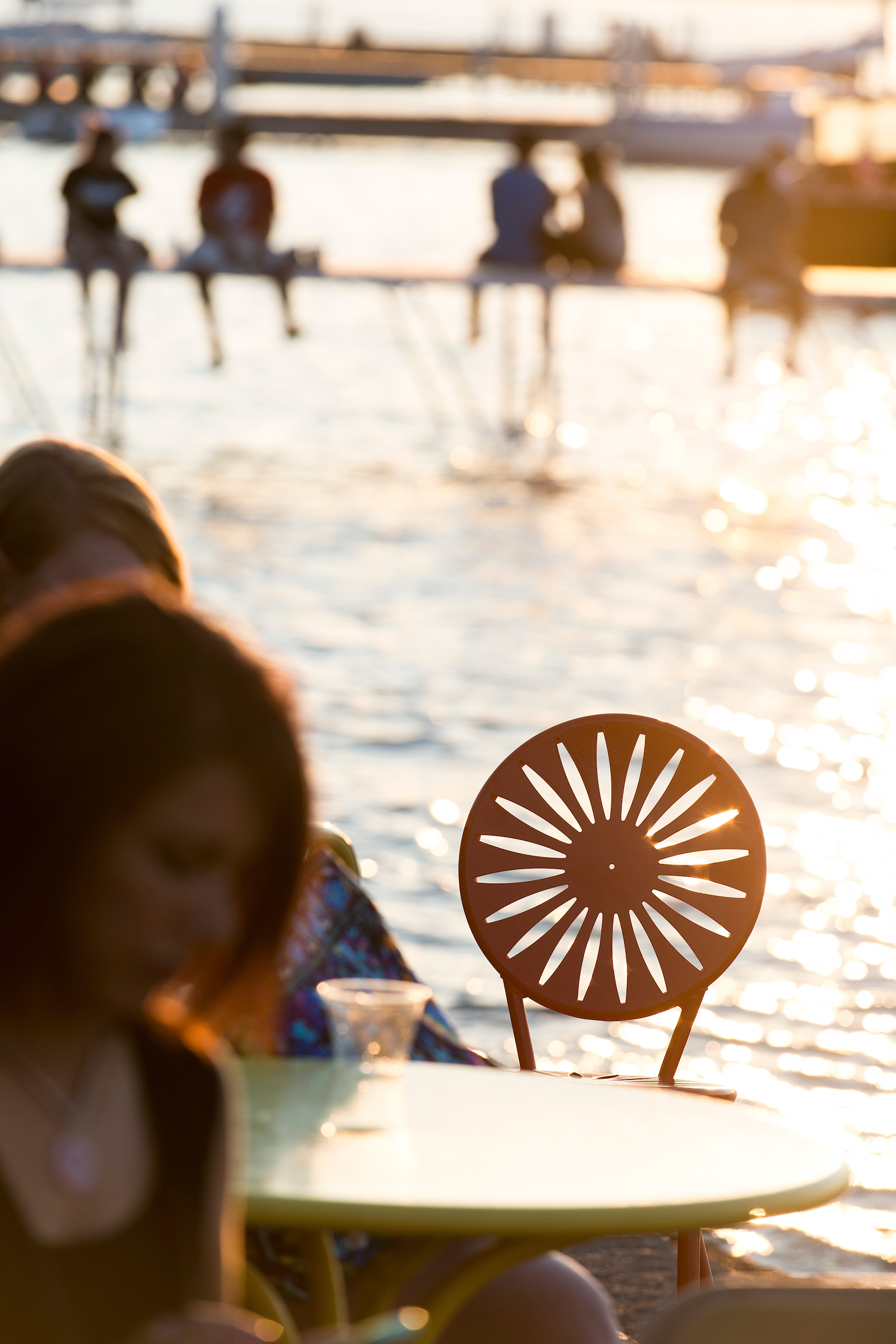 Photo of people sitting on metal sun styled chairs on the waterfront.